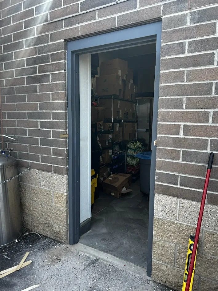 New dark blue-grey steel door frame going into the opening in a concrete block wall, with the door leaf not yet hung and buckets inside