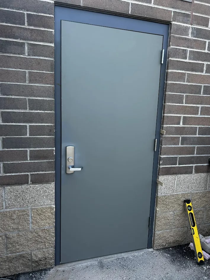 New grey hollow metal back service door hung in its new dark steel frame with a brushed lever handle and lock, exterior view