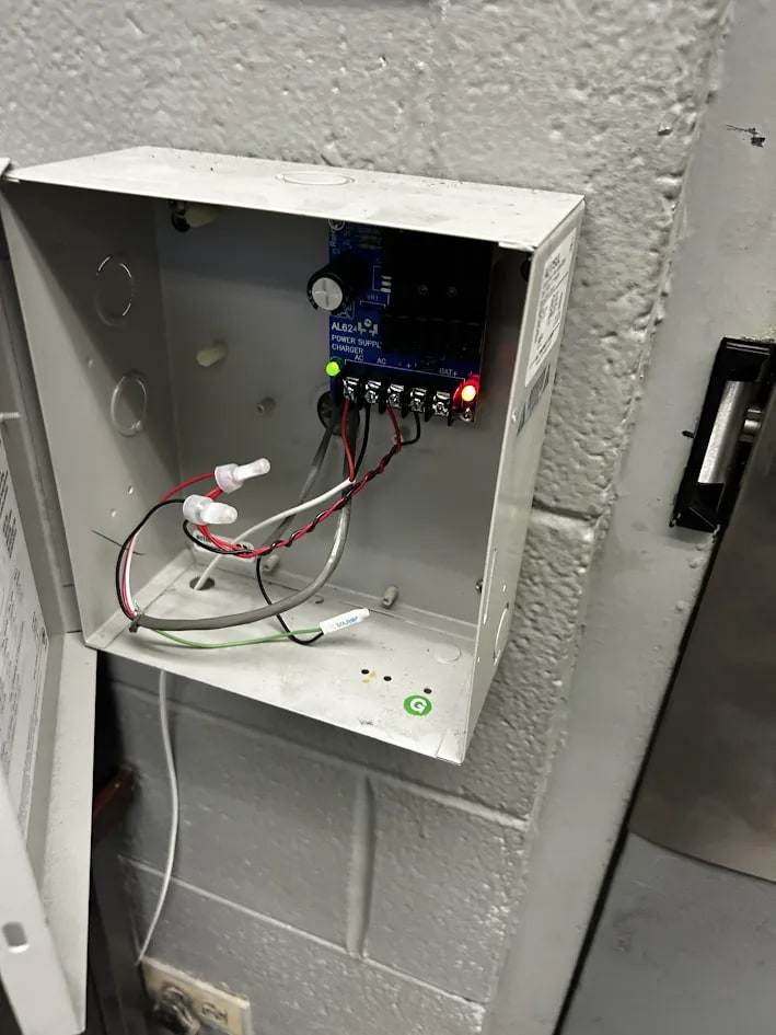 Control enclosure open to show the power supply board, terminal wiring and two illuminated status lamps, with the door jamb at right