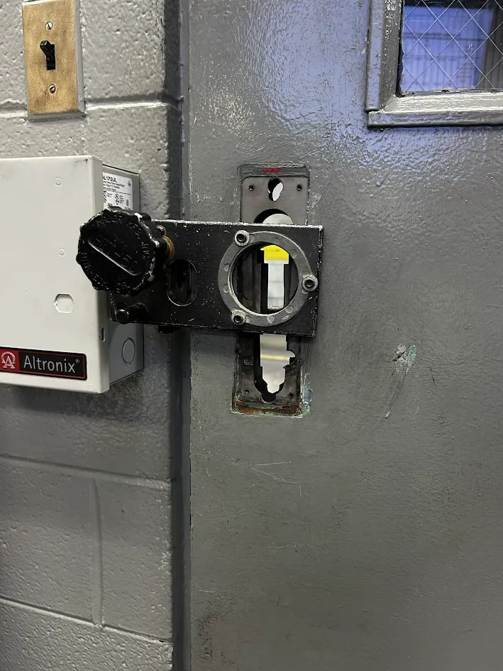 Steel door with a black strike body offered up at the latch line and a galvanised plate alongside