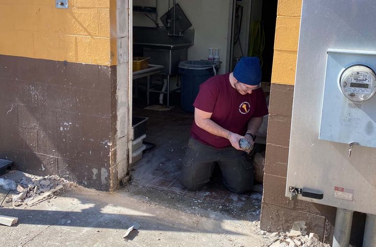 Man kneeling at a commercial doorway with tools beside an electric meter box