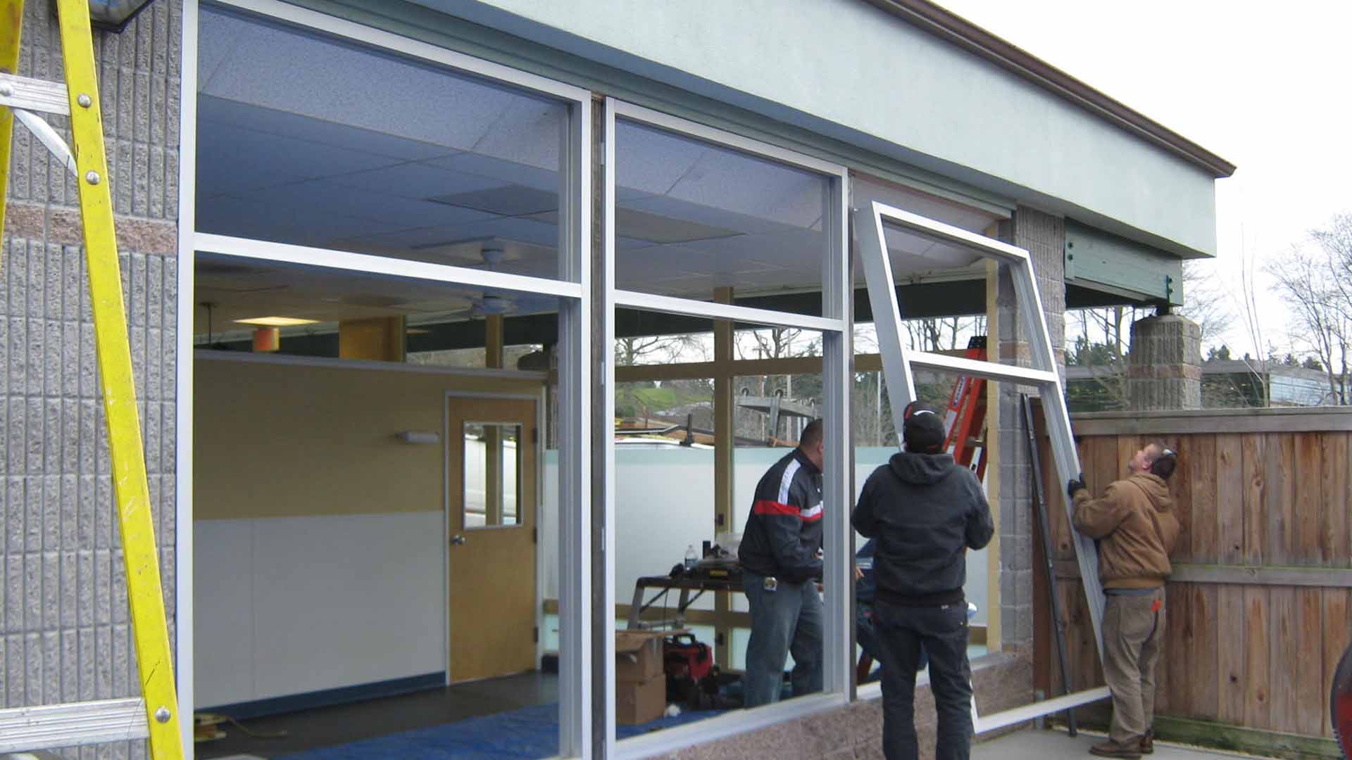 Workers installing a new aluminum framed glass storefront window during an exterior building renovation