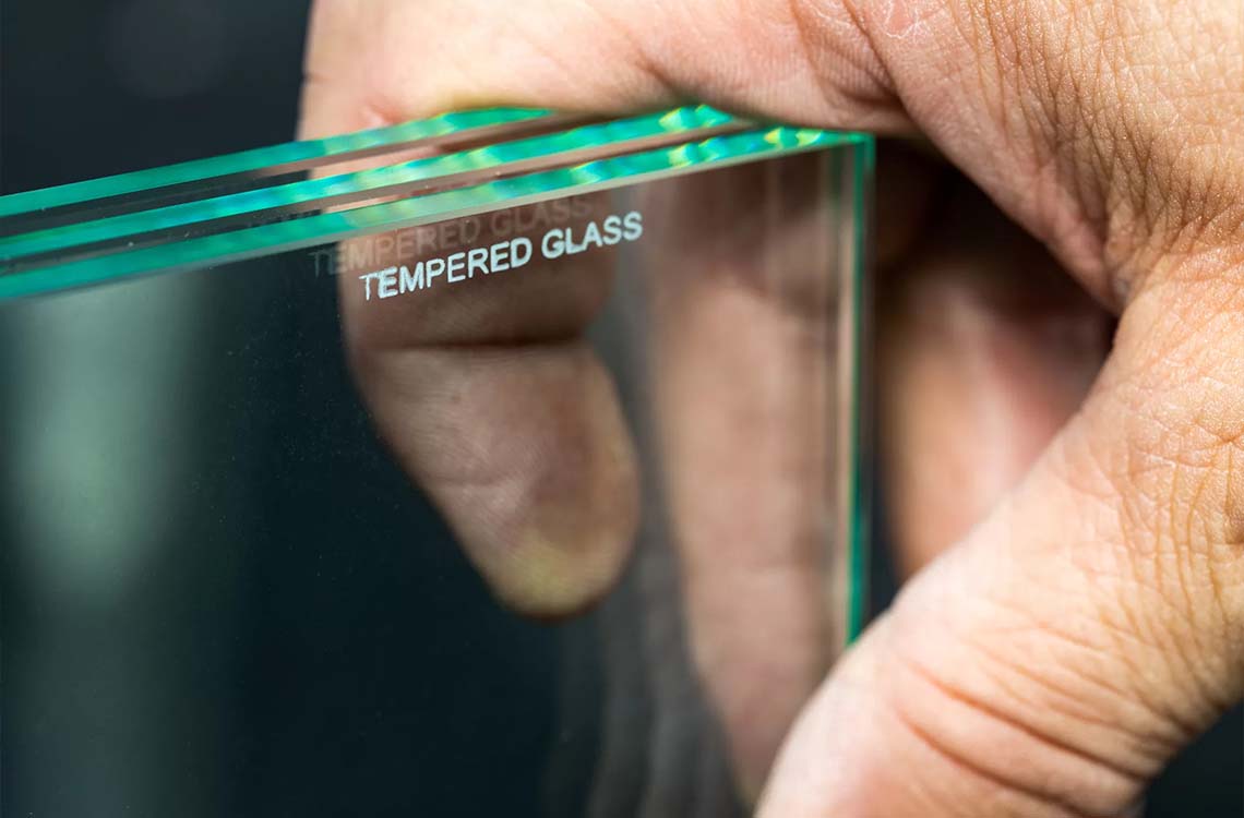 Close up of hands holding a glass pane edge printed with the words TEMPERED GLASS