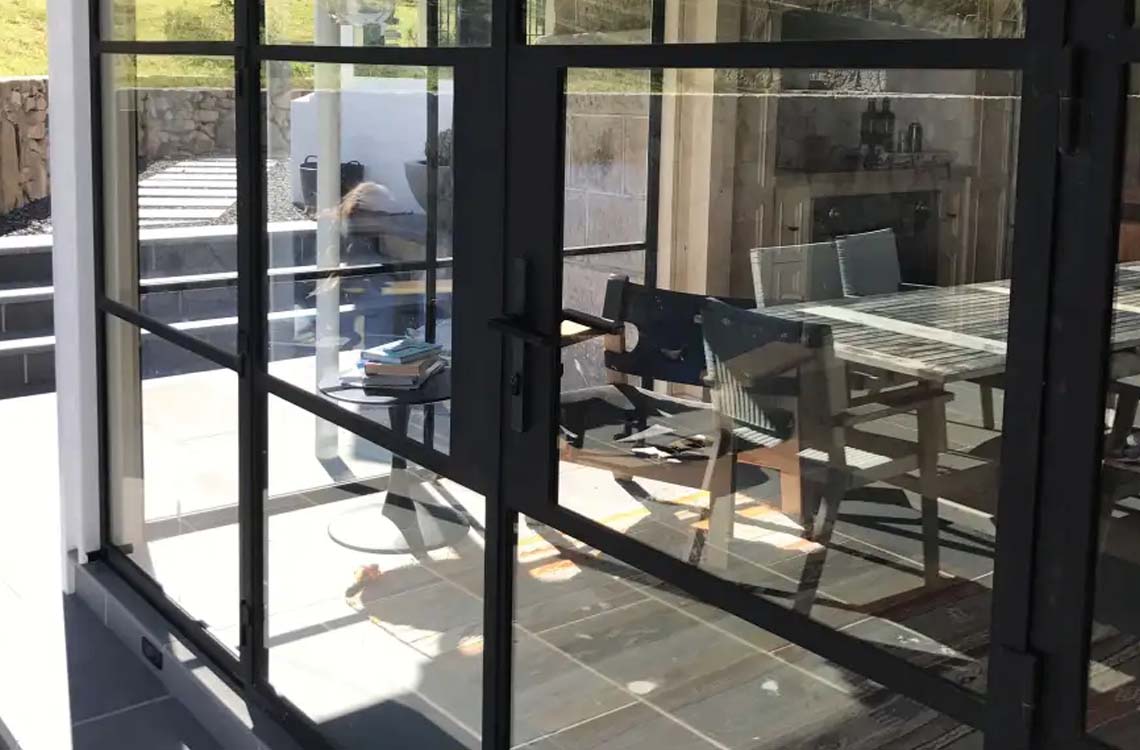 Black steel framed patio doors with glass panels looking onto an outdoor dining table and chairs