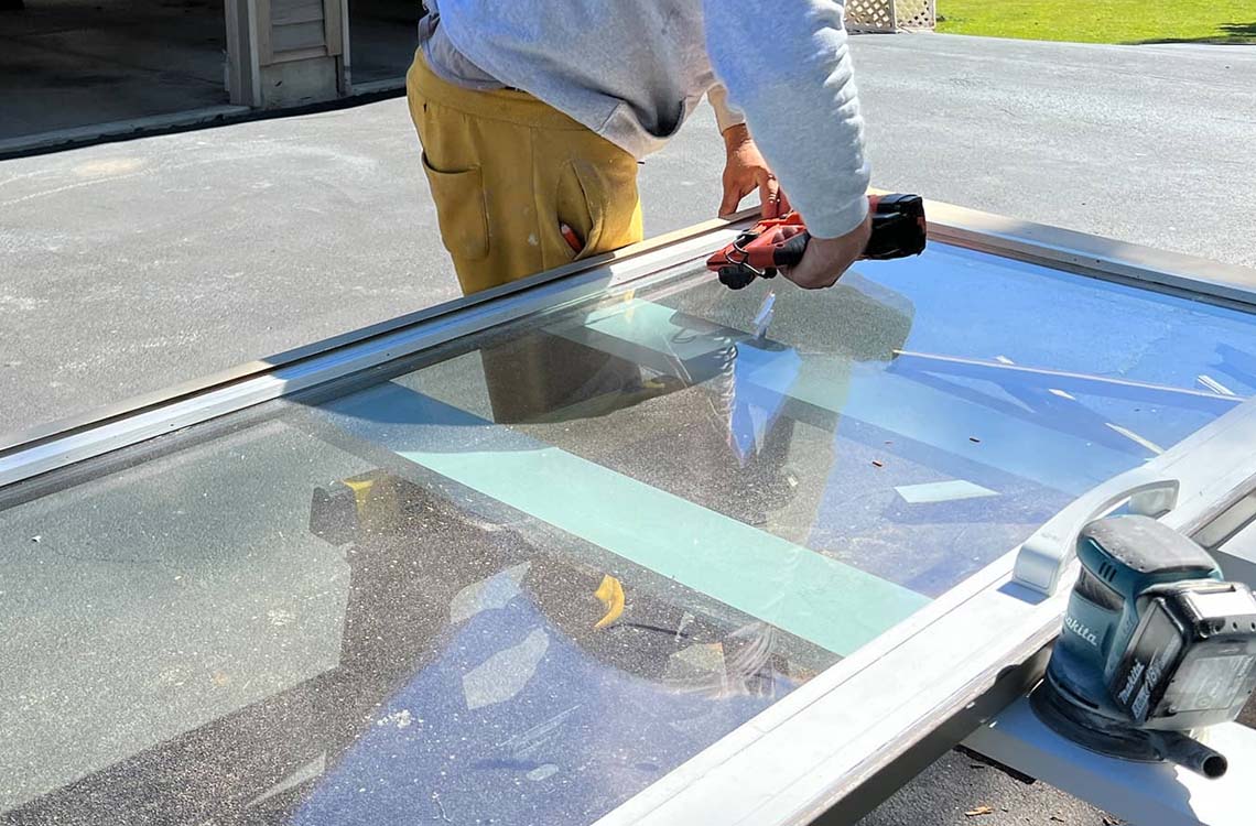 Person running a power tool along the edge of a glass panel on a work table outdoors