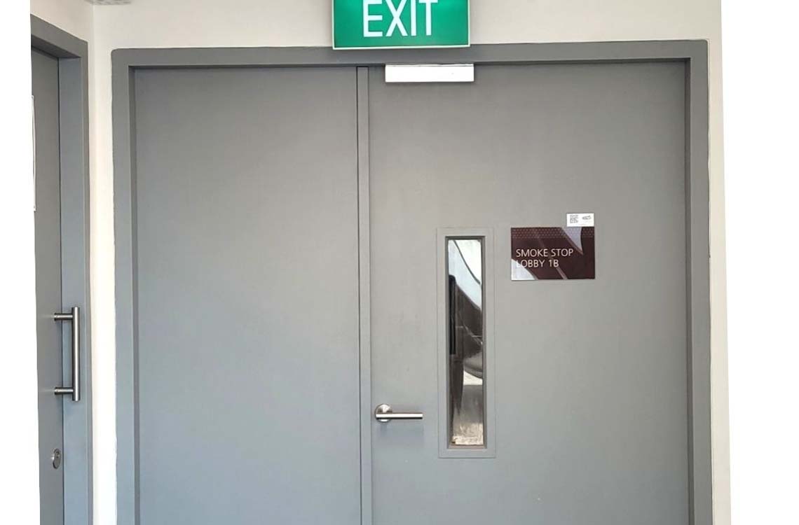 Gray metal exit door with narrow glass vision panel and smoke stop lobby sign