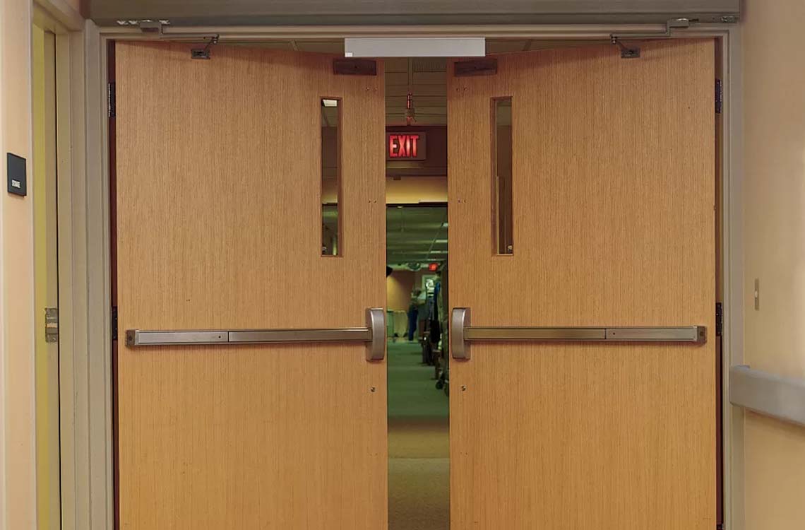 Wooden double doors with metal push bars and red EXIT sign in hallway