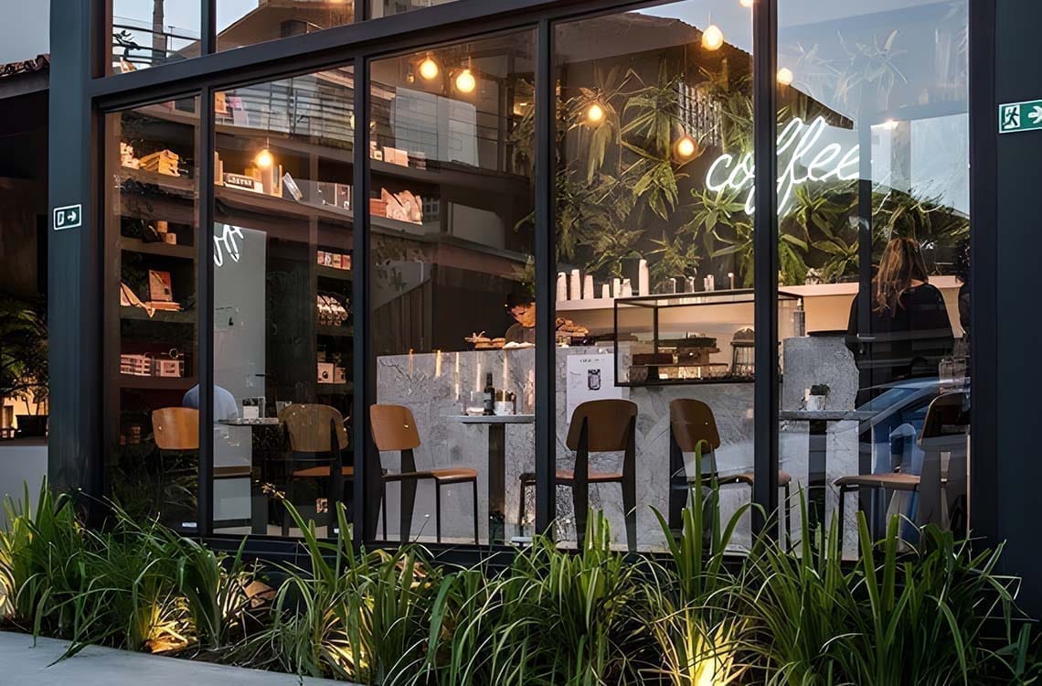 Black metal framed glass restaurant facade with neon coffee sign and plants