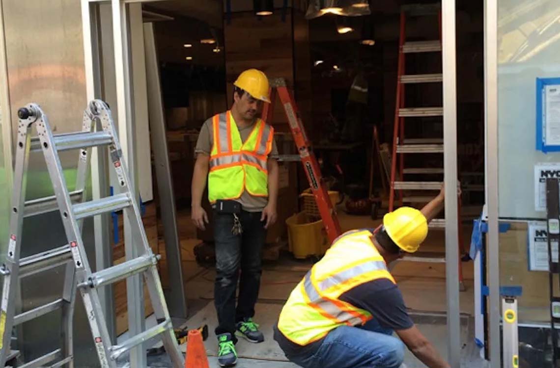 Workers in hard hats and safety vests installing glass storefront door frames