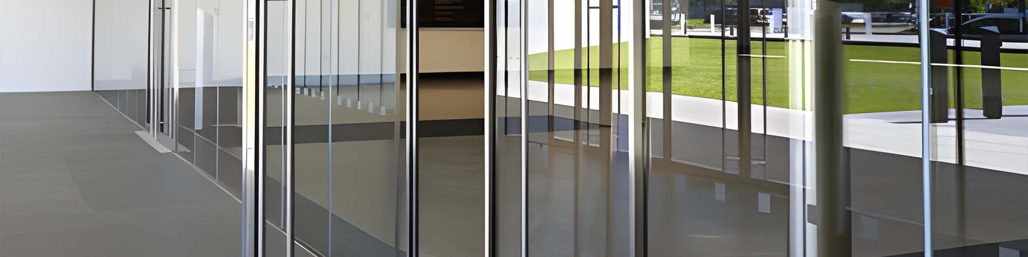 Tinted glass entry wall reflecting green lawn and gray paved walkway