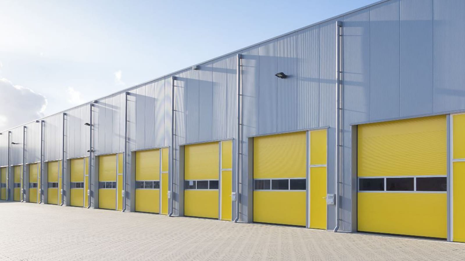 Row of yellow overhead sectional doors along a metal clad warehouse exterior