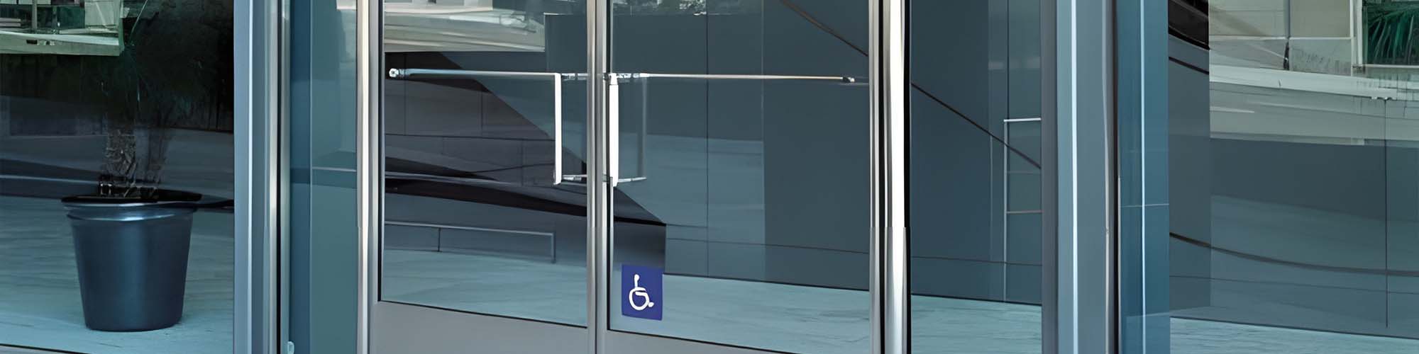 Glass entrance doors with push bar hardware and blue wheelchair access sign