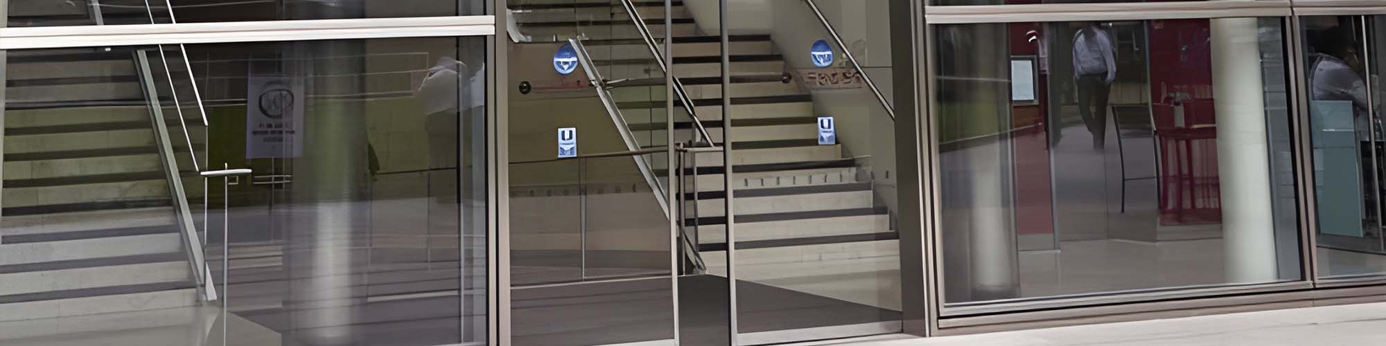 Glass storefront panels reflecting an indoor staircase, elevator signs and pedestrians