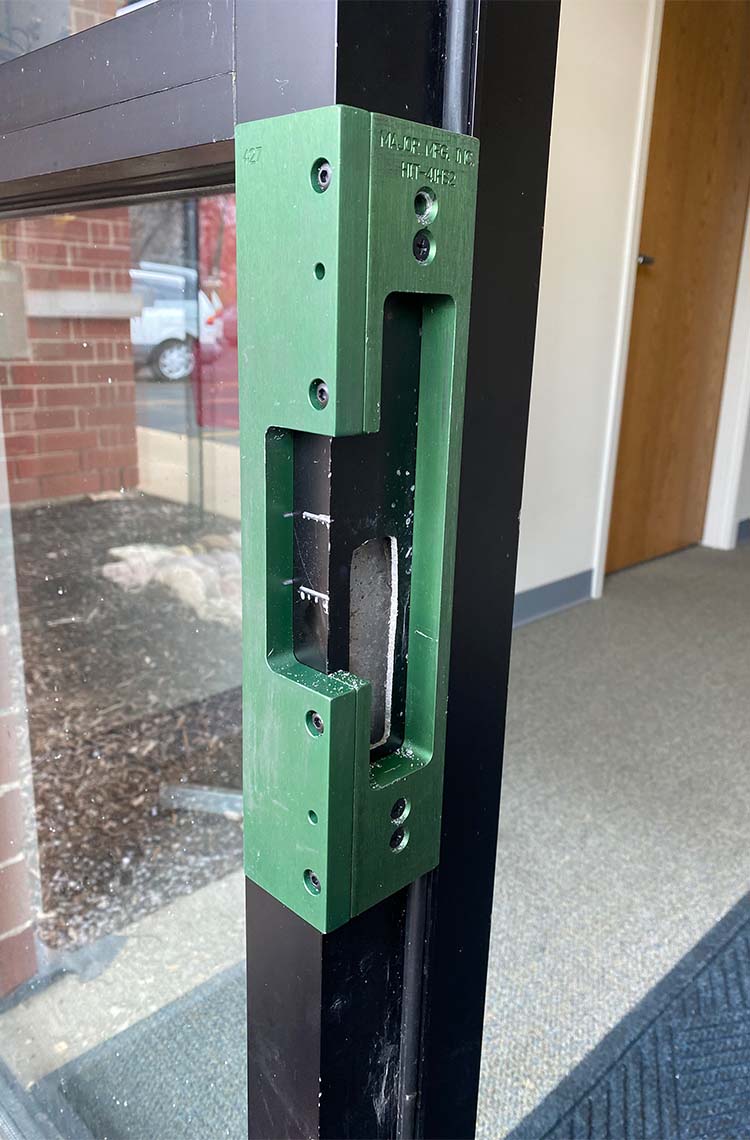 Green electric strike plate set into a black metal storefront door frame