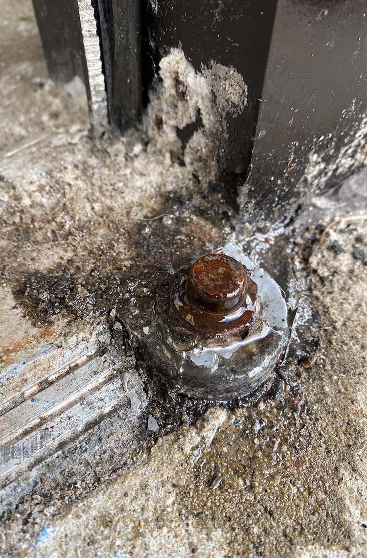 Rusted floor bolt and sealant at the base of a black exterior door frame