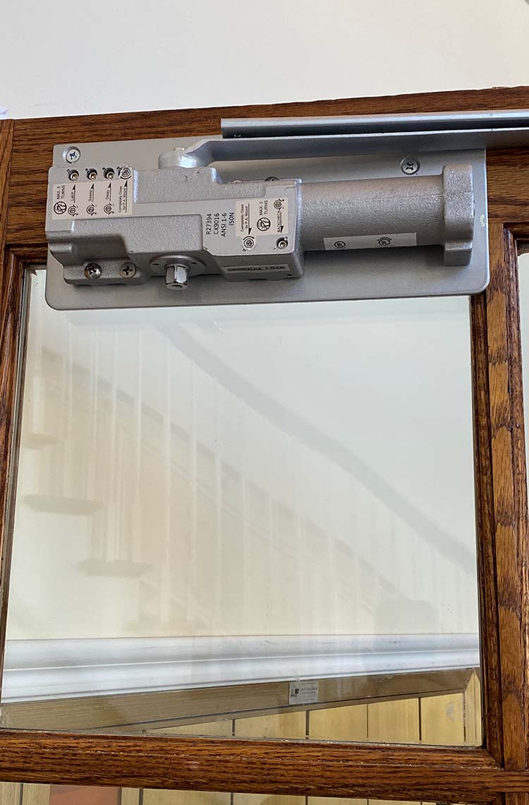 Overhead hydraulic door closer mounted on a wood framed glass door
