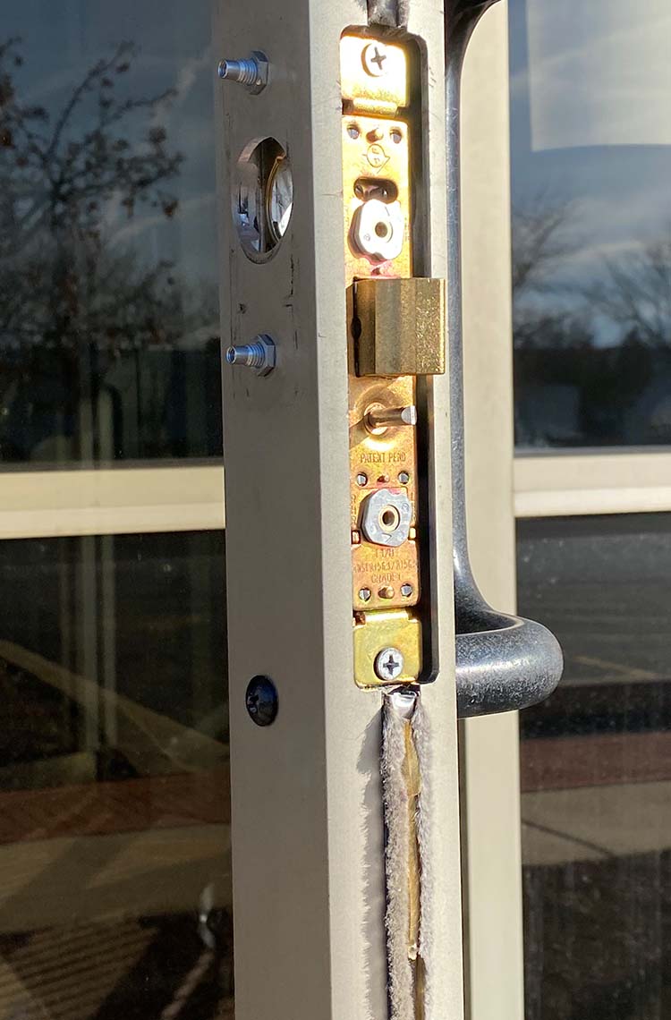 Mortise lock faceplate and brass deadbolt on aluminum storefront door