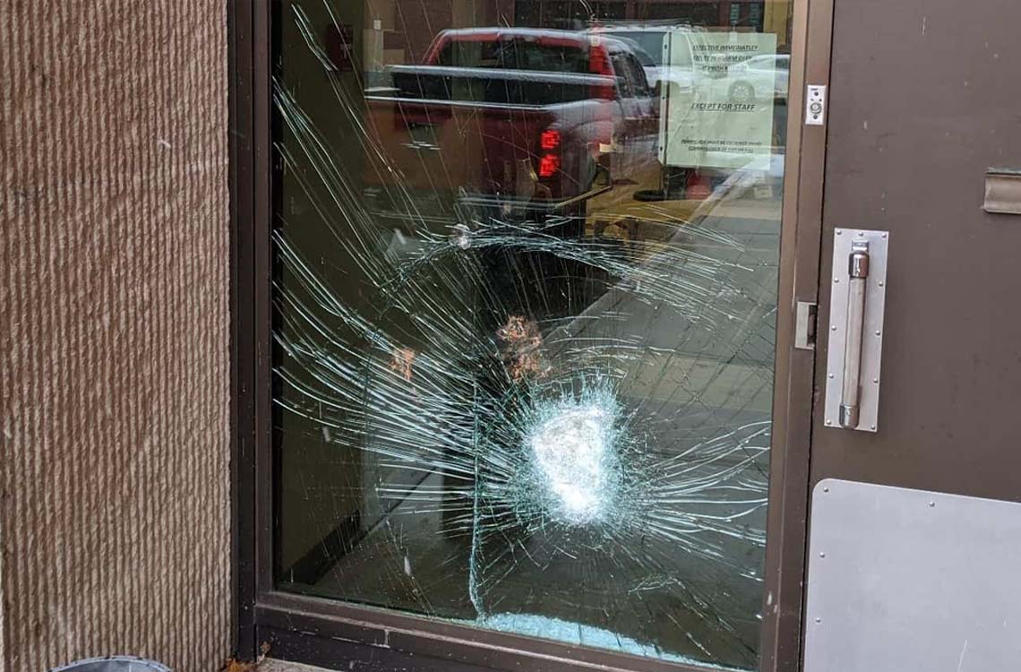 Shattered tempered glass storefront door panel with impact break and parking lot behind
