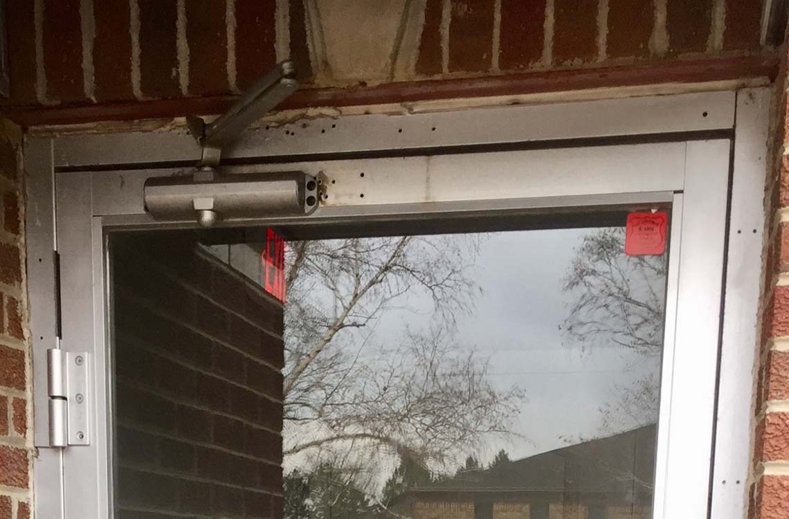 Commercial door closer mounted above aluminum storefront door frame on brick wall