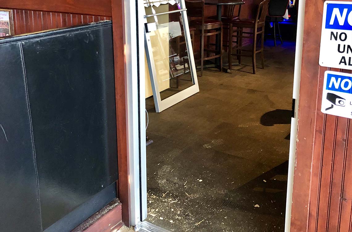 Interior commercial doorway with paneled wall, bar stools and wood debris on floor