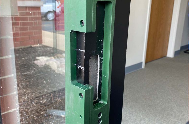 Green painted steel door frame with recessed cutout beside glass and brick