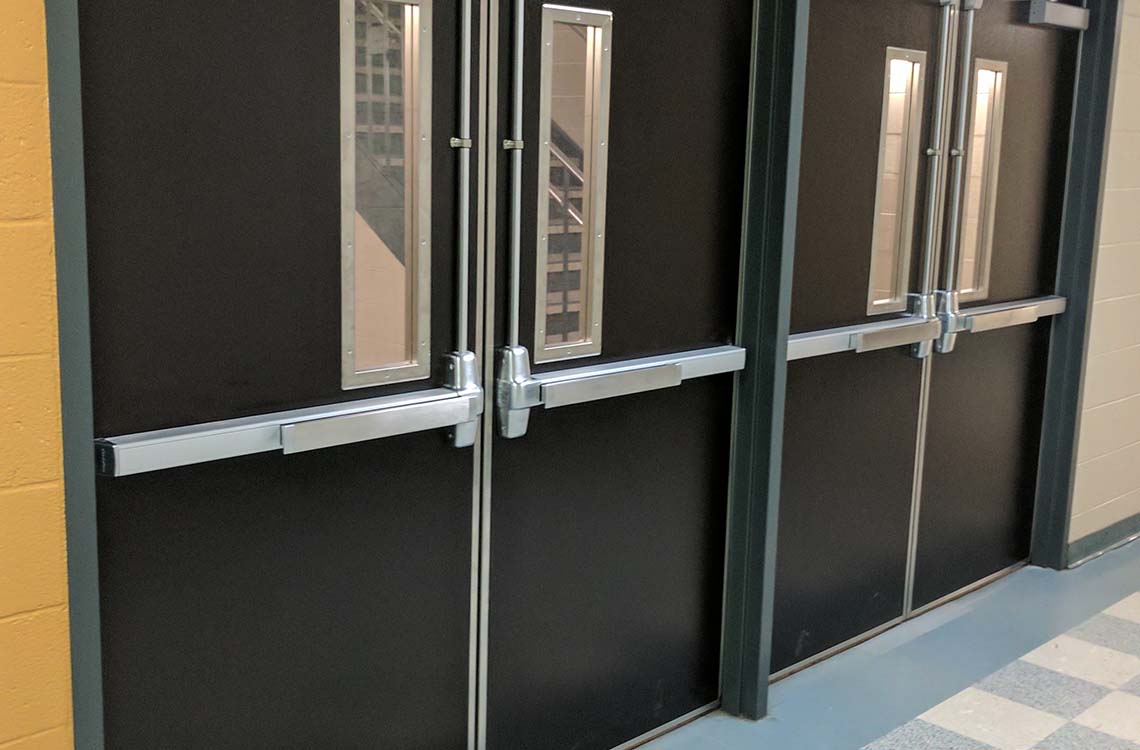 Metal exit doors with push bars and narrow windows in block hallway