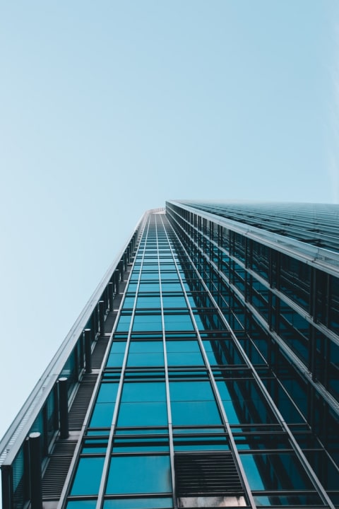 Upward view of a glass and steel office tower against pale blue sky