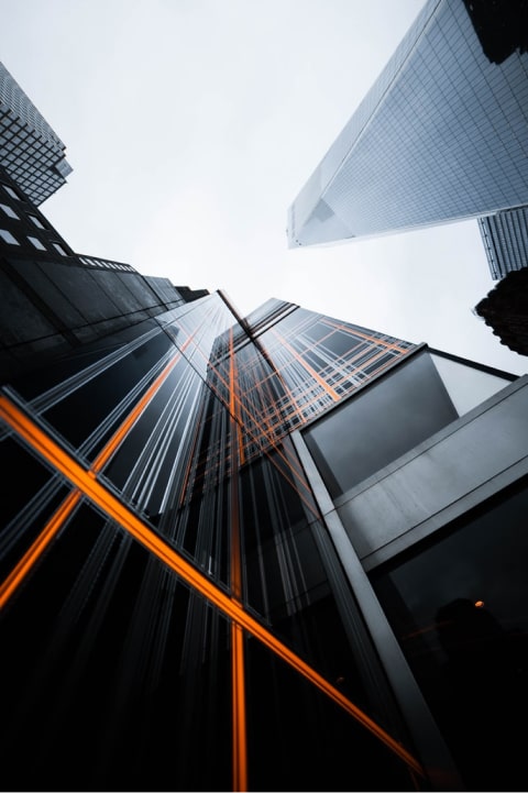Low angle view of glass skyscrapers reflecting orange light streaks, overcast sky