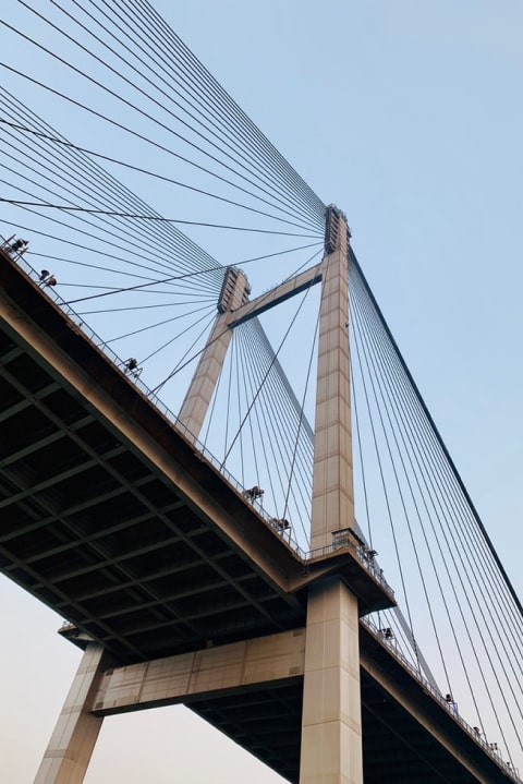 Looking up at concrete bridge tower with diagonal steel cables, blue sky