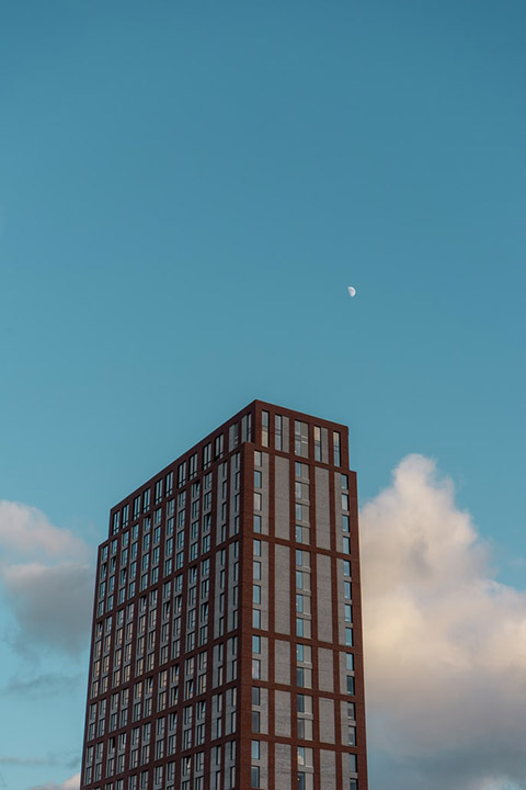 Brick and glass apartment tower below a crescent moon in blue sky