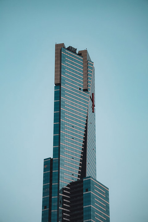 Tall glass office skyscraper with stepped upper floors against hazy sky